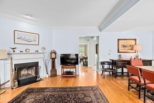 living area with a fireplace with flush hearth, ornamental molding, and wood finished floors