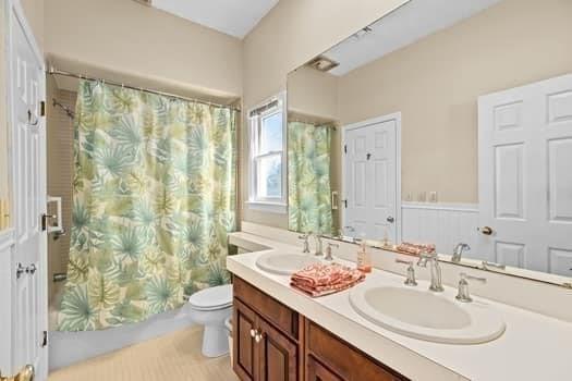 bathroom featuring double vanity, toilet, a sink, and shower / tub combo with curtain