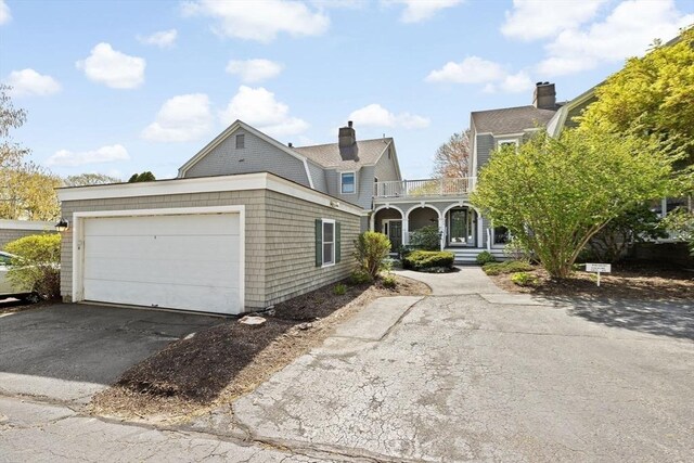 shingle-style home with a garage, aphalt driveway, a balcony, and covered porch
