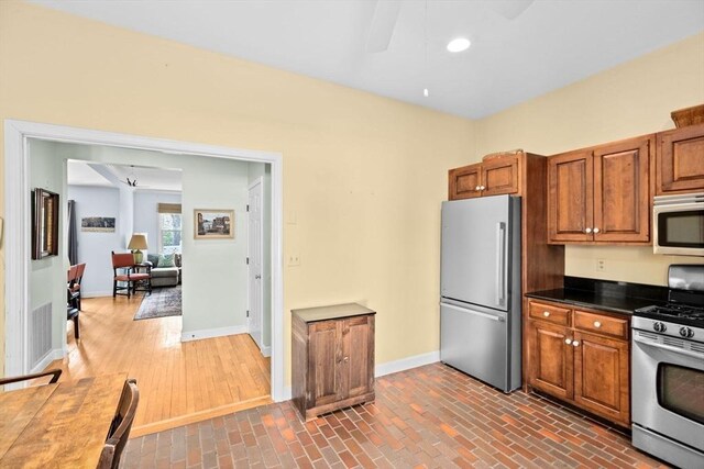 kitchen featuring dark countertops, brown cabinetry, stainless steel appliances, a ceiling fan, and baseboards