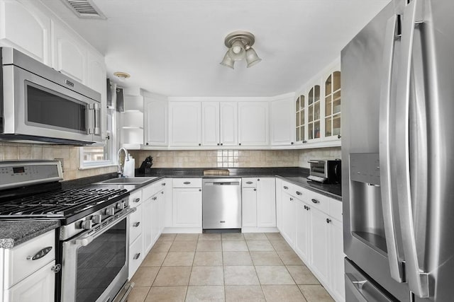 28 Chestnut St, Falmouth, MA 02536 - kitchen featuring appliances with stainless steel finishes, light tile patterned flooring, decorative backsplash, and glass insert cabinets