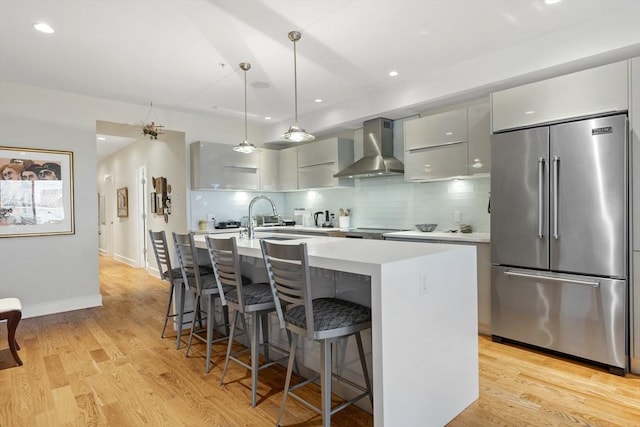 kitchen with light wood-style flooring, high end fridge, light countertops, wall chimney exhaust hood, and modern cabinets