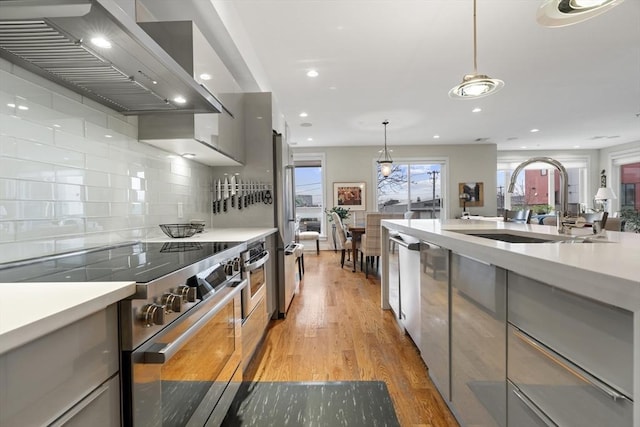 kitchen featuring wall chimney range hood, light countertops, premium appliances, light wood-style floors, and a sink