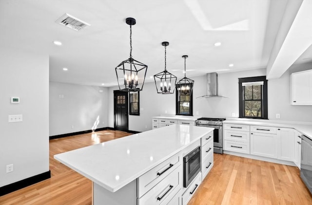 kitchen featuring light countertops, a kitchen island, appliances with stainless steel finishes, wall chimney range hood, and visible vents