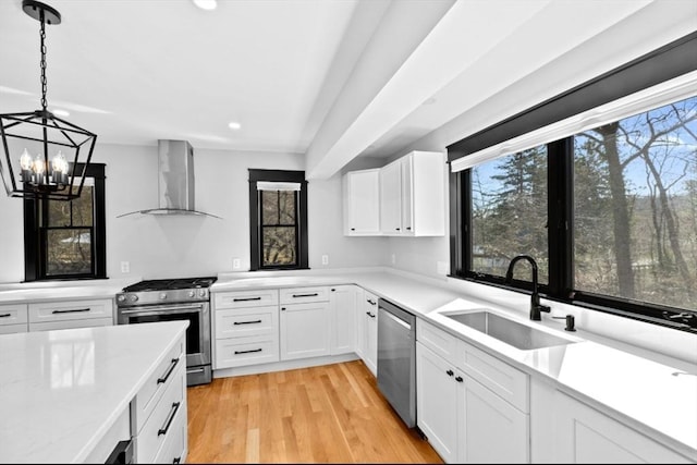 kitchen with a sink, wall chimney range hood, a healthy amount of sunlight, and appliances with stainless steel finishes