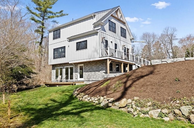 back of property with stone siding, board and batten siding, a deck, and a yard