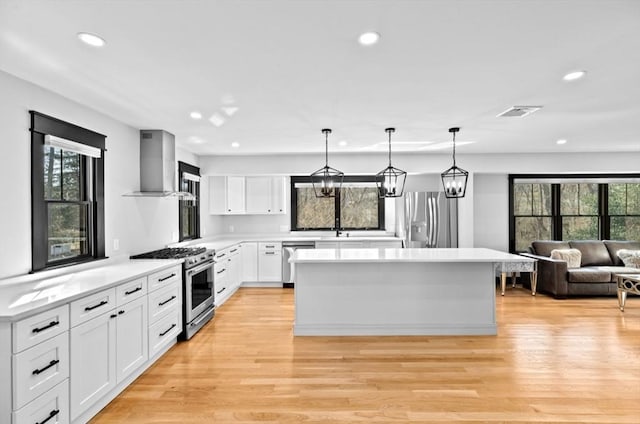 kitchen featuring light countertops, wall chimney exhaust hood, a kitchen island, appliances with stainless steel finishes, and light wood-style floors