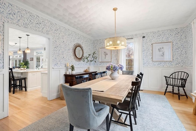 dining space with ornamental molding, a wainscoted wall, wallpapered walls, and light wood-style floors