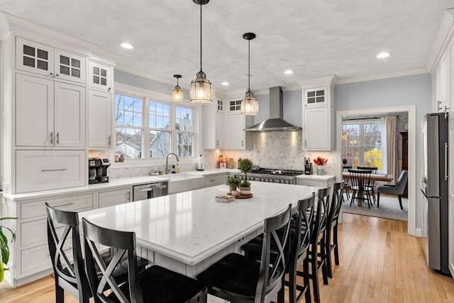 kitchen featuring wall chimney exhaust hood, a sink, white cabinetry, and light countertops