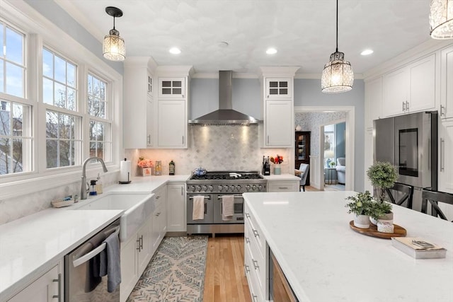 kitchen with light wood-style floors, appliances with stainless steel finishes, wall chimney range hood, and white cabinetry