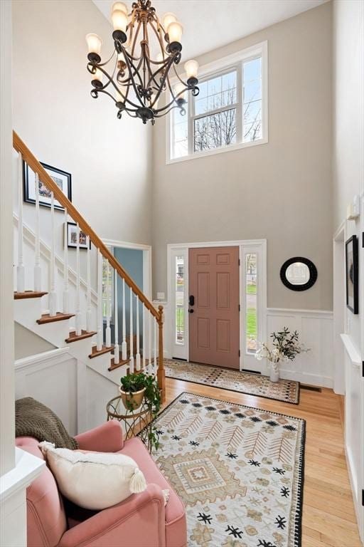 entrance foyer featuring stairway, a wainscoted wall, light wood-type flooring, a notable chandelier, and a high ceiling