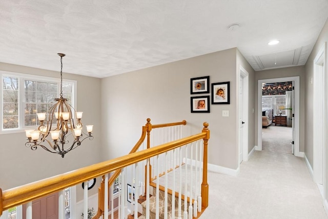 hallway featuring attic access, a chandelier, an upstairs landing, light carpet, and baseboards