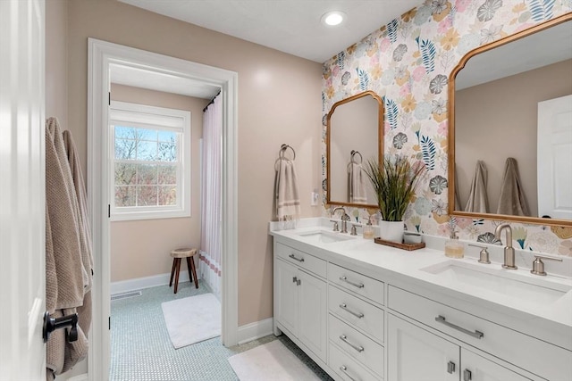 bathroom with double vanity, a sink, wallpapered walls, and baseboards