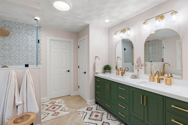full bath featuring baseboards, tiled shower, double vanity, and a sink