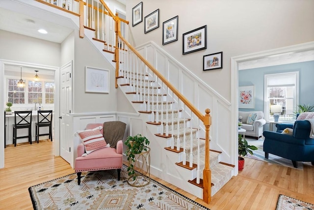 stairway with a towering ceiling, wood finished floors, and a decorative wall