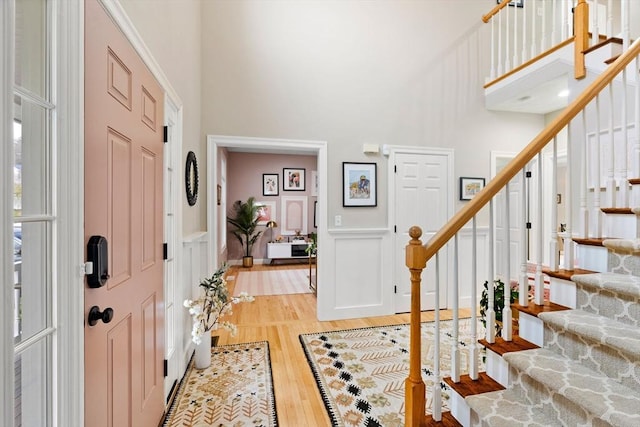 entryway with a towering ceiling, light wood finished floors, stairway, and a decorative wall