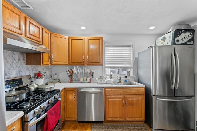 kitchen with light wood-type flooring, stainless steel appliances, tasteful backsplash, and sink