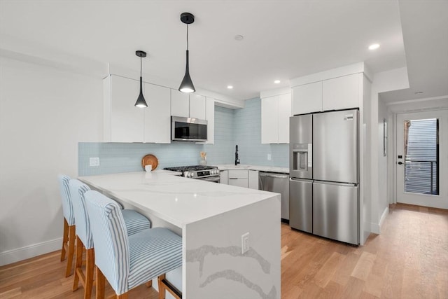 kitchen with kitchen peninsula, appliances with stainless steel finishes, white cabinetry, and hanging light fixtures