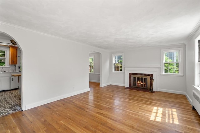 31 Whitman Ave, Melrose, MA 02176 - unfurnished living room featuring arched walkways, light wood finished floors, plenty of natural light, a brick fireplace, and crown molding