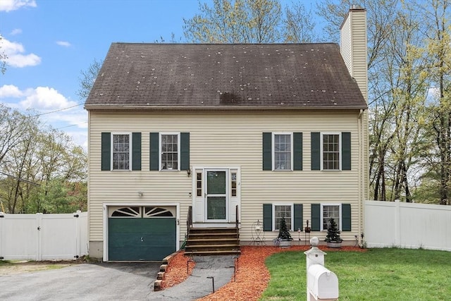 view of front facade featuring an attached garage, asphalt driveway, a chimney, and a gate