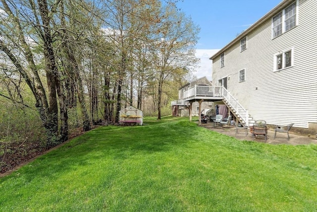 view of grassy yard featuring a deck, a patio, stairway, and an outbuilding