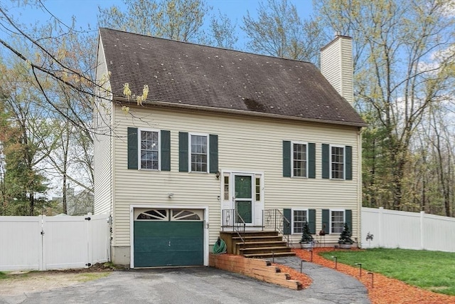 view of front of home featuring a garage, driveway, a chimney, and fence