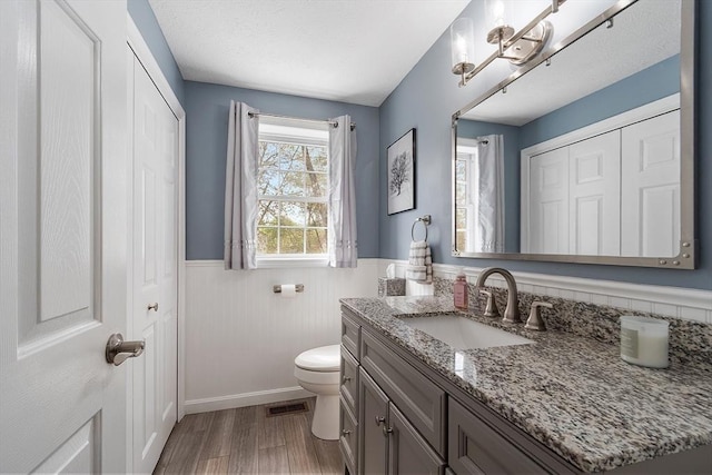 bathroom featuring a wainscoted wall, toilet, vanity, wood finished floors, and a chandelier