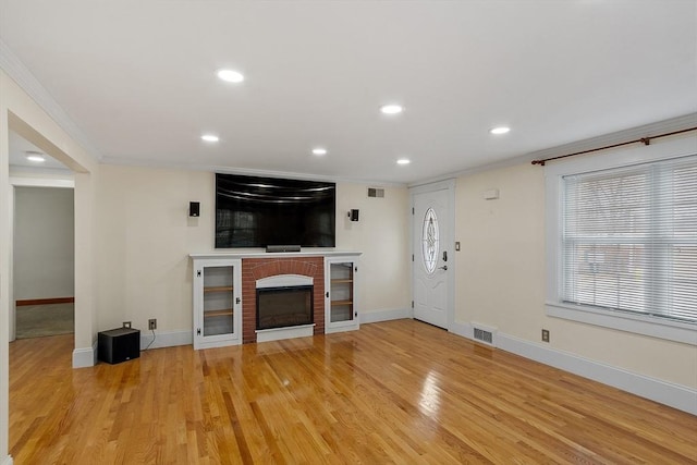 unfurnished living room featuring a fireplace, ornamental molding, and light wood-type flooring