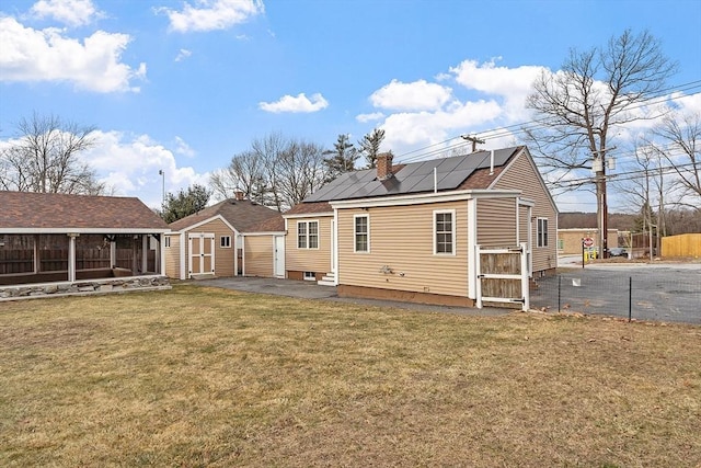 rear view of property with solar panels, a storage shed, and a yard