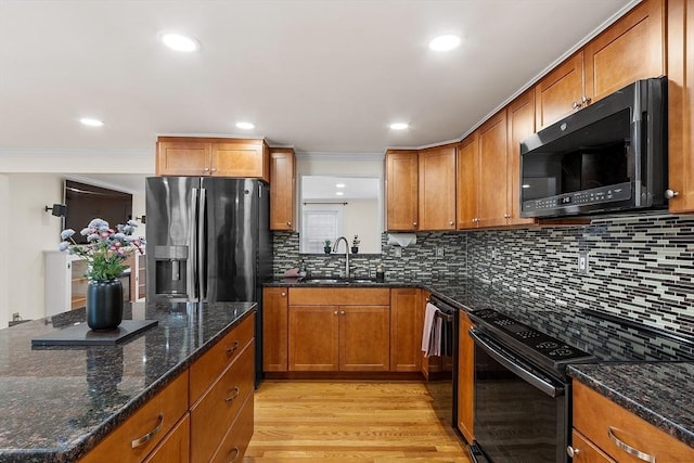 kitchen featuring sink, backsplash, dark stone countertops, black appliances, and light wood-type flooring