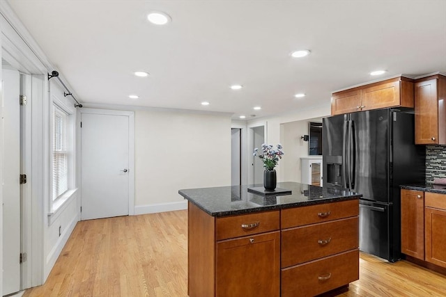 kitchen with black refrigerator with ice dispenser, backsplash, dark stone counters, a kitchen island, and light wood-type flooring