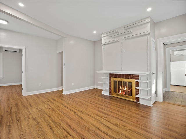 unfurnished living room featuring a wall mounted AC, a fireplace, and wood-type flooring