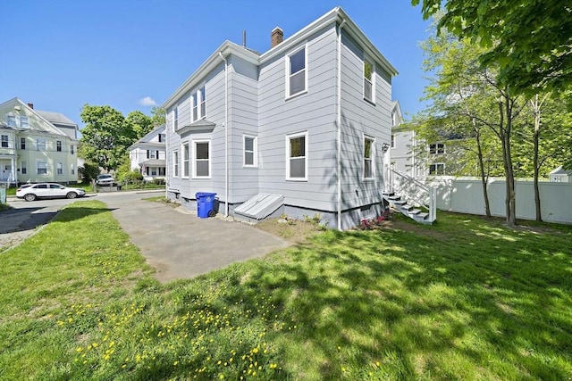 rear view of house with a chimney, fence, and a lawn