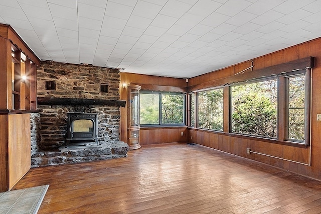 unfurnished living room with a wood stove, wooden walls, and hardwood / wood-style flooring