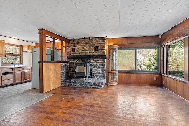 unfurnished living room with sink, wood walls, a wood stove, and wood-type flooring