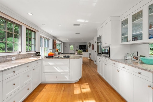 kitchen featuring stainless steel microwave, light stone countertops, glass insert cabinets, and white cabinets