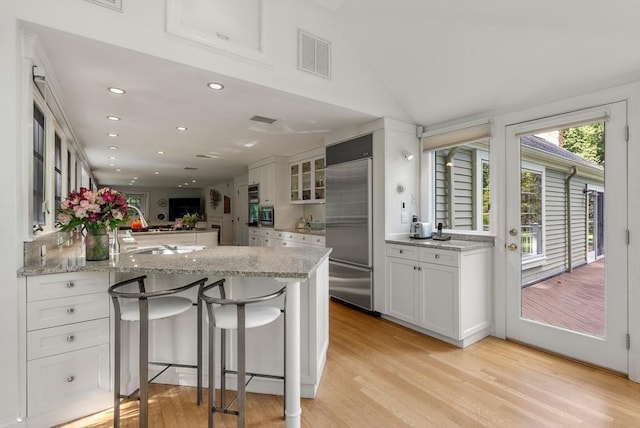 kitchen featuring glass insert cabinets, a peninsula, light stone countertops, built in refrigerator, and white cabinetry