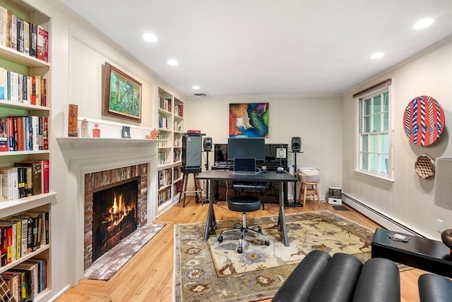 office featuring light wood-style flooring, ornamental molding, a brick fireplace, built in shelves, and a baseboard heating unit