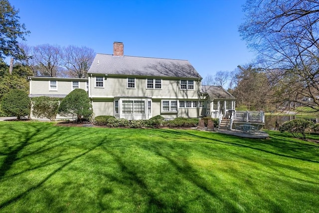 rear view of property with a chimney, a deck, and a lawn