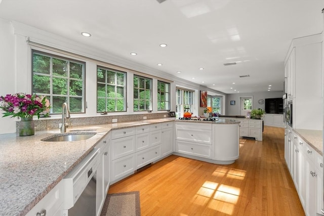 kitchen featuring white cabinets, dishwashing machine, a peninsula, light stone countertops, and a sink