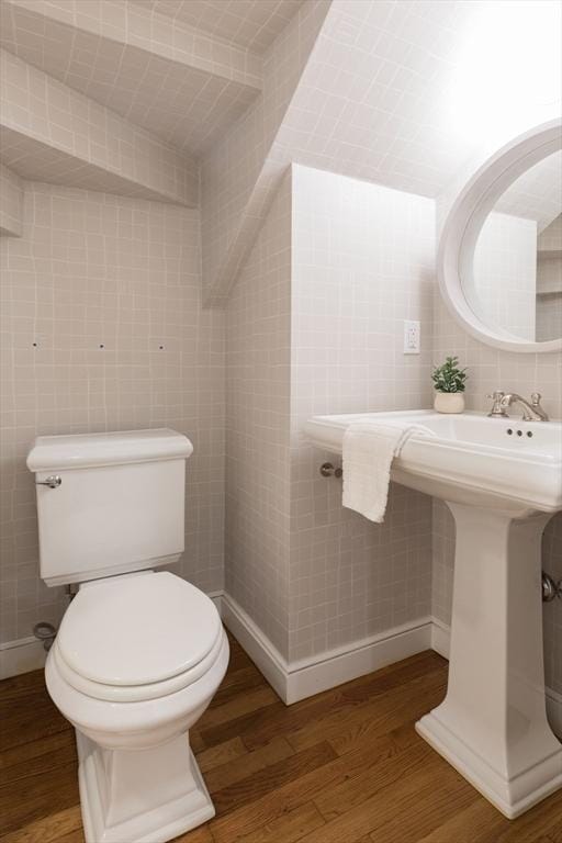 half bathroom with wood finished floors, toilet, and tile walls