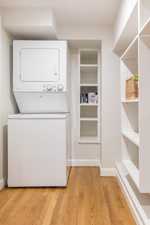 laundry room with baseboards, stacked washer and dryer, light wood-style flooring, and laundry area