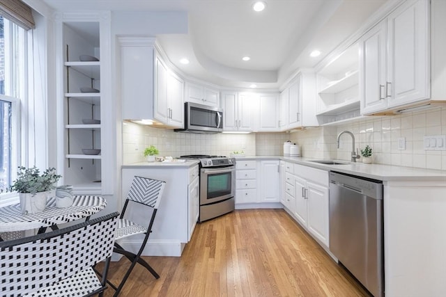 kitchen with white cabinets, open shelves, appliances with stainless steel finishes, a sink, and light countertops