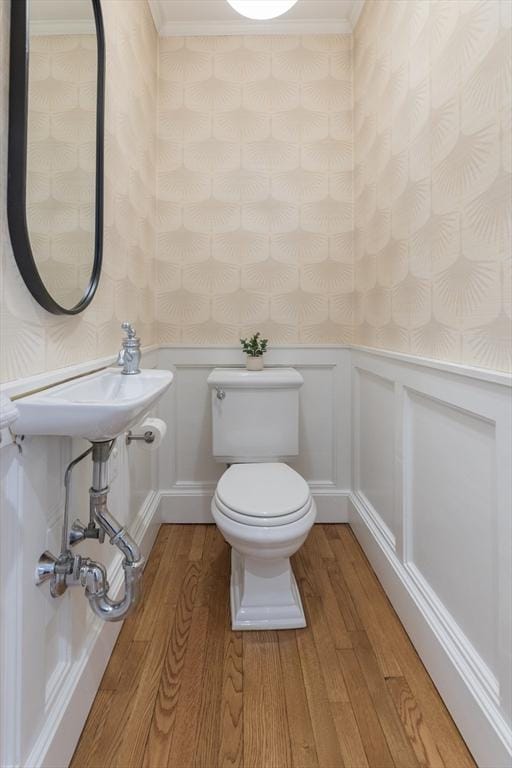 half bath with a wainscoted wall, toilet, wallpapered walls, and wood finished floors