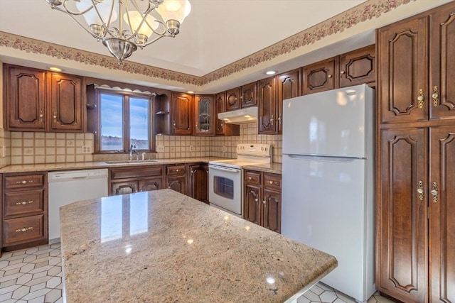 kitchen with decorative backsplash, a sink, a chandelier, under cabinet range hood, and white appliances