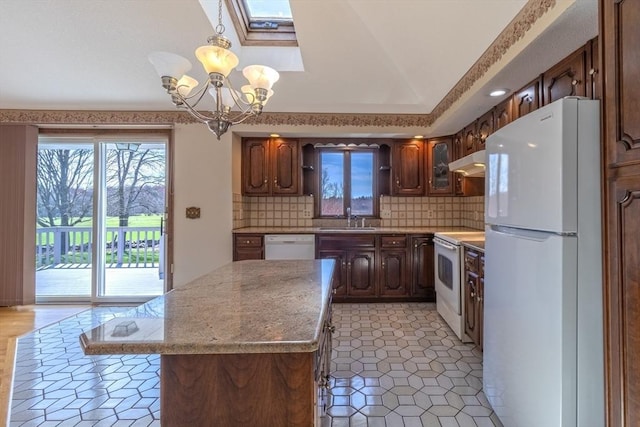 kitchen with an inviting chandelier, a sink, under cabinet range hood, white appliances, and a skylight