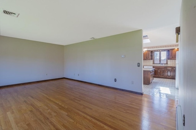 empty room featuring a sink, visible vents, wood finished floors, and baseboards