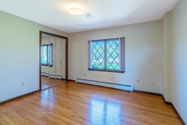 unfurnished bedroom with a baseboard heating unit, visible vents, and light wood-type flooring