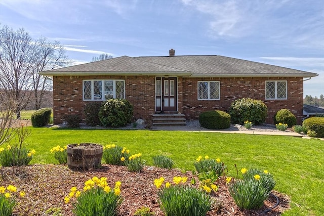 ranch-style home with entry steps, a chimney, roof with shingles, a front yard, and brick siding