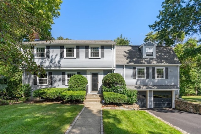 colonial inspired home with aphalt driveway, a garage, and a front lawn